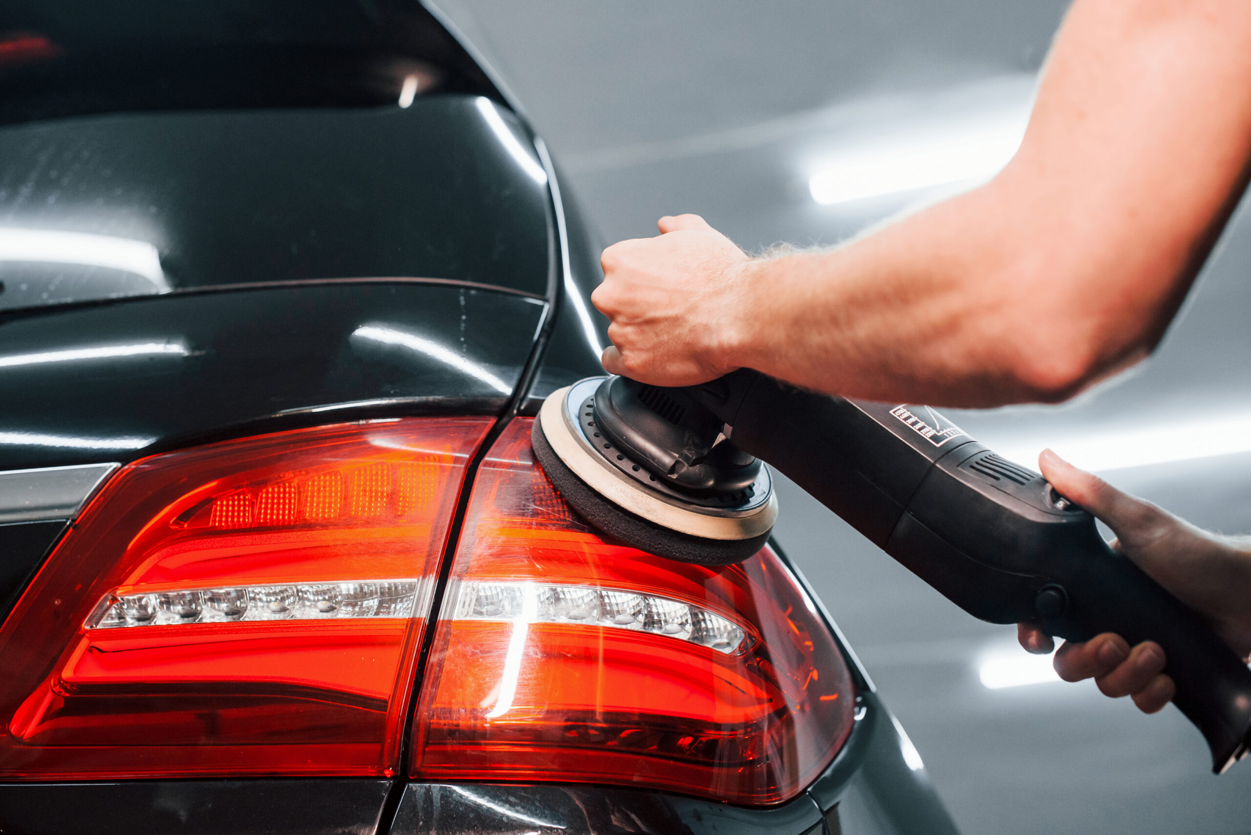 Guy polishing surface of vehicle. Modern black automobile get cleaned by man inside of car wash station.